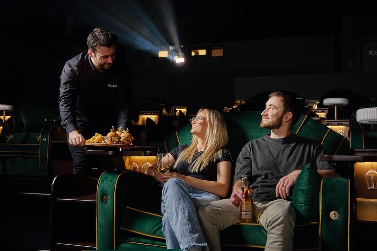 Waiter serving food to a couple in plush green velvet seats inside The Piccadilly cinema auditorium in North Adelaide.